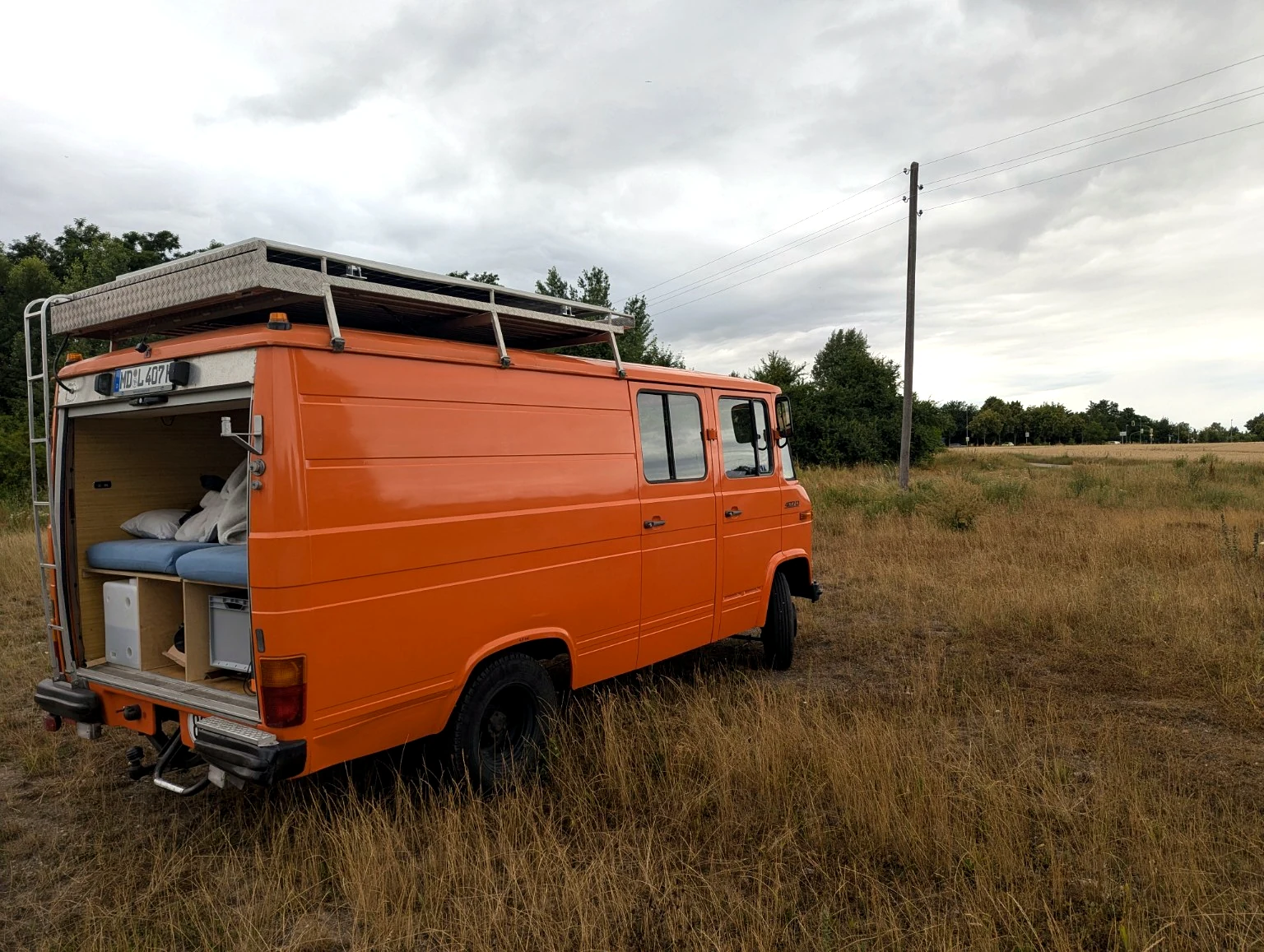 Orangefarbener Düdo mit geöffnetem Heck, sichtbar sind Bett und Stauraum