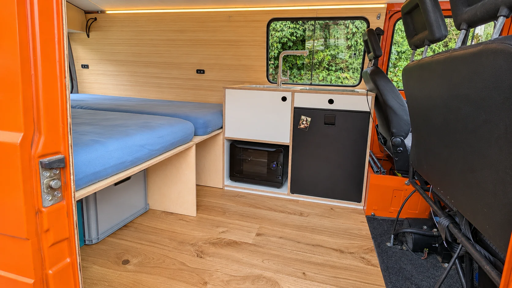 Blick durch die offene Seitentür auf Bett, Küchenzeile und Stauraum